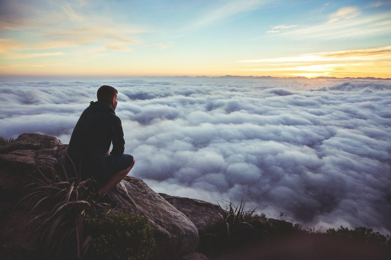 man sitting on gray rock while staring at white clouds scaled 1